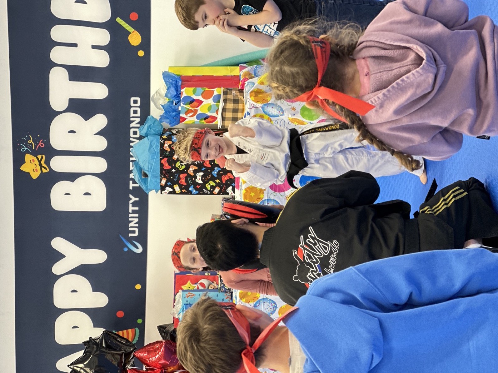Birthday child celebrating with friends in front of the Happy Birthday banner at a Unity Taekwondo birthday party in Chilliwack